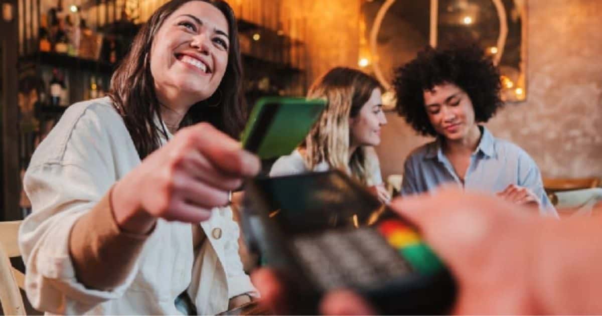 Een jonge dame rekent af met haar betaalkaart via de mobiele betaalterminal die gekoppeld is aan het kassasysteem van de horecazaak waar ze met haar twee vriendinnen op café ging.