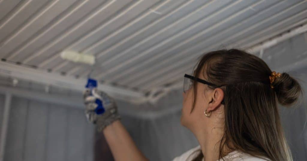 Een professionele schilder schildert het plafond van een woning met witte verf.