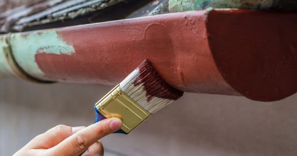 Detailbeeld van een verweerde dakgoot die rood of bordeaux wordt geschilderd met een verfborstel.