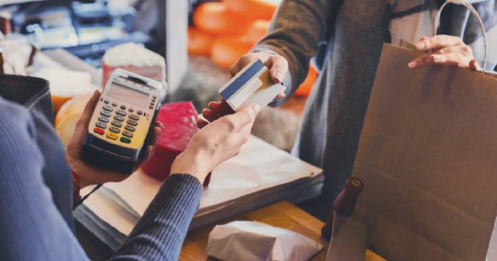 Een klant geeft haar kaart aan een winkelbediende die een mobiele betaalterminal vasthoudt.