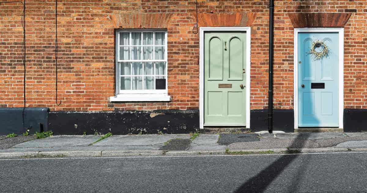 Twee voordeuren in dezelfde stijl: de ene in het lichtblauw, de andere lichtgroen. Het verschil tussen beide deuren zit hem in de details. Bij de blauwe deur hangt er een krans van wildbloemen op en is de brievenbus iets breder. Terwijl bij de groene deur niet echt versiering ophangt.