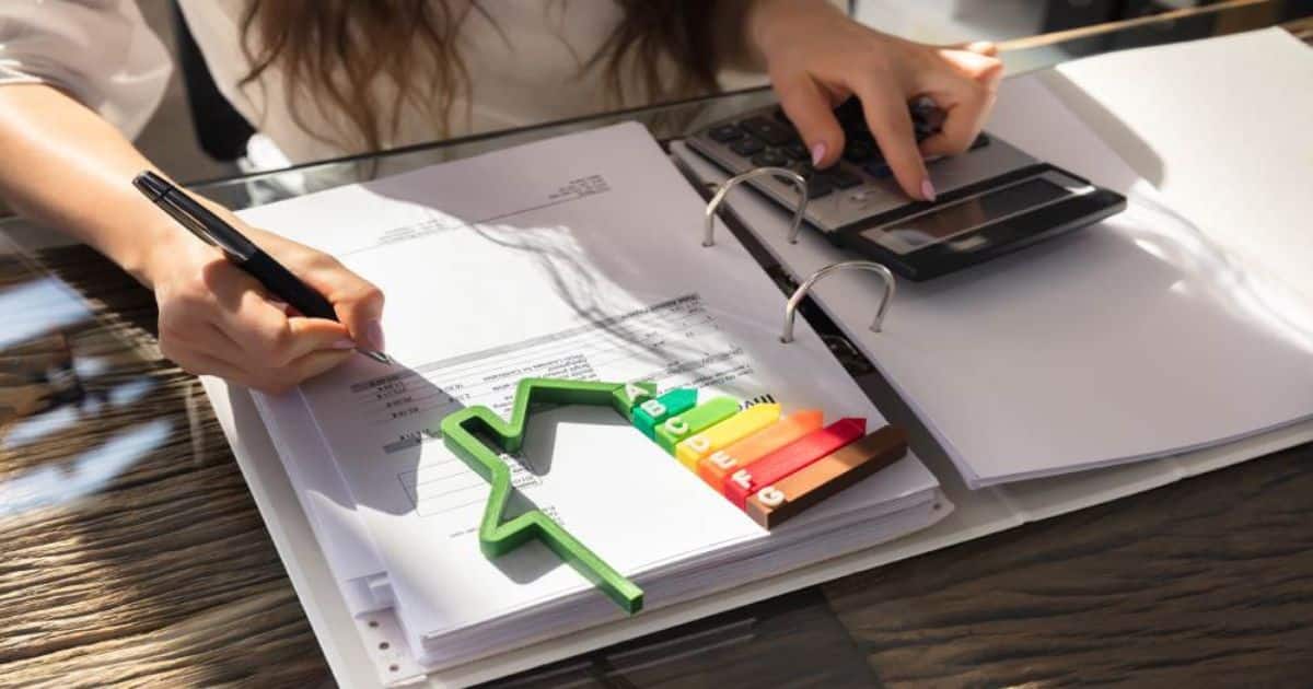 Iemand werkt aan documenten met een rekenmachine, erop ligt een energielabel in kleuren van A tot G.