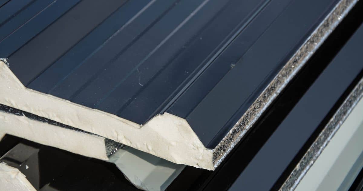 Doorsnede van een sandwichpaneel: een donkerblauwe toplaag met ondiep trapeziumstructuur, een isolerende kernlaag, en een vlakke onderlaag.