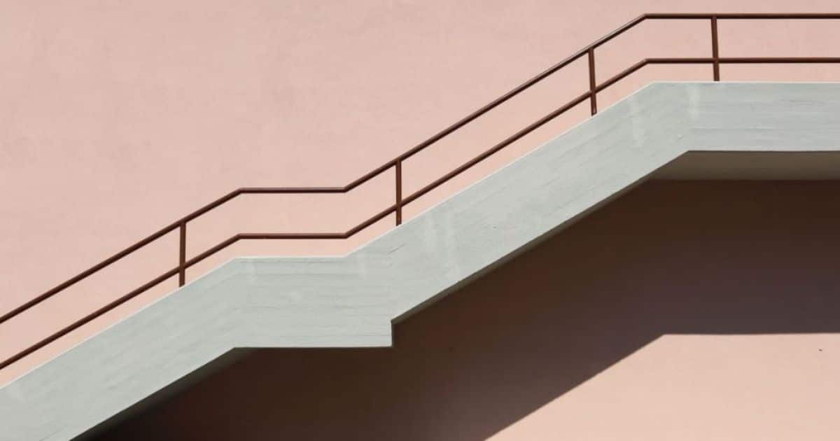 Bordestrap tegen een zalmrozige muur. De trap heeft een donkerbruine leuning. 