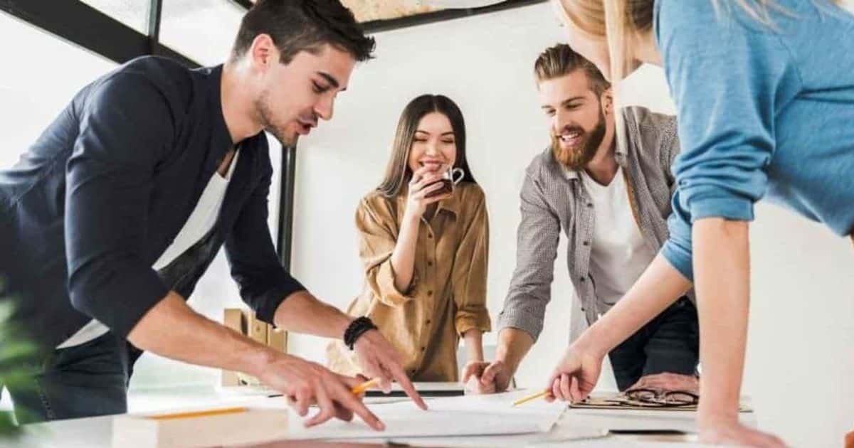 Twee mannen en twee vrouwen staan rond een tafel met papieren. Ze zijn in de weer met het vergelijken van sociale secretariaten. De achterste vrouw drinkt thee uit een doorzichtige tas.