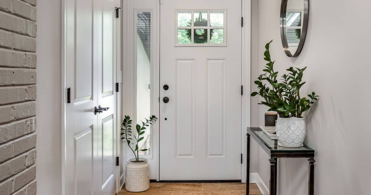 Een gezellig ingerichte hal met spiegel, planten op verschillende hoogtes, een tafeltje voor sleutels en een inbouwkast. Buiten aan de voordeur hangt ook nog een groene krans.