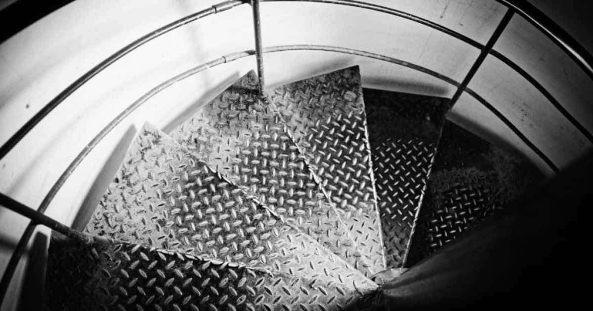 Metalen spiltrap die naar de kelder gaat. De foto is in zwart-wit.