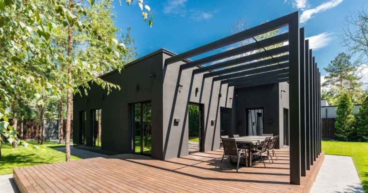 Een zwarte moderne woning met overkapt houten terras en een ruime tuin.