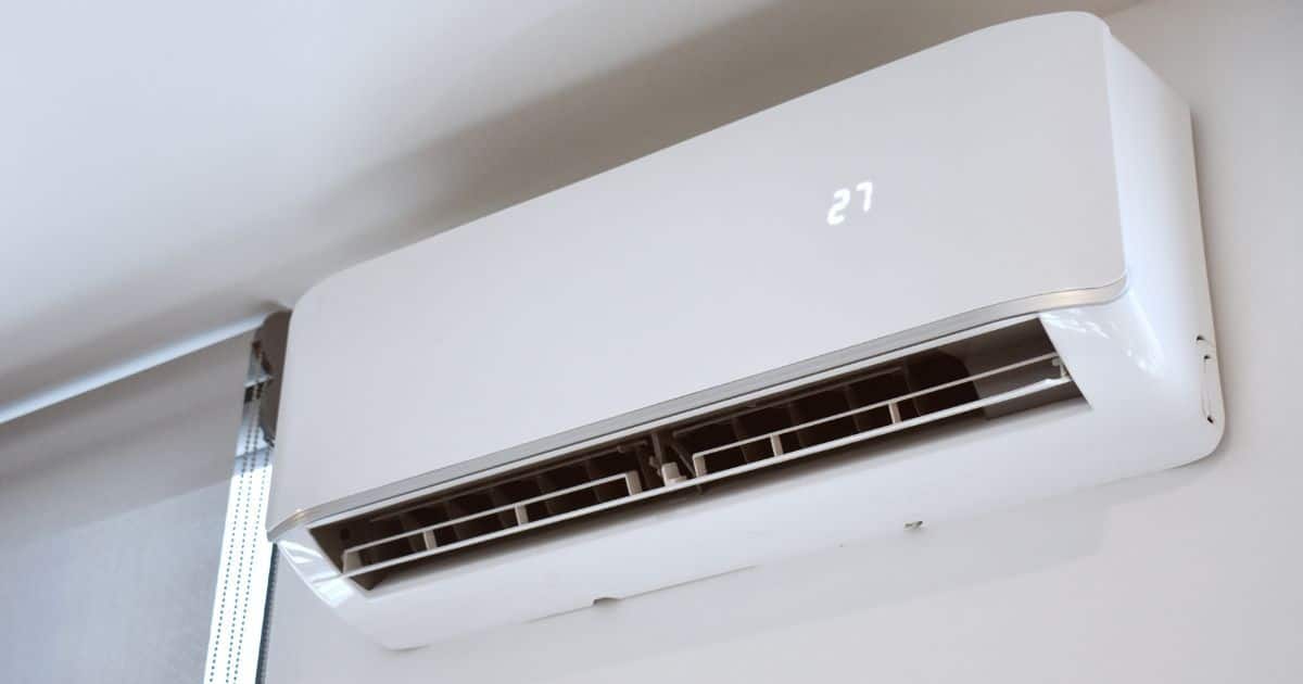 Witte monoblock airco die op 27 graden staat en op de wand is gemonteerd, net onder het plafond en aan het venster.