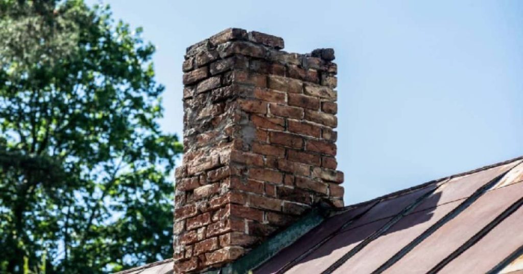 Een verweerde bakstenen schouw die duidelijk al een paar stenen heeft verloren. Het dak zelf is van bruinig of rood zink.