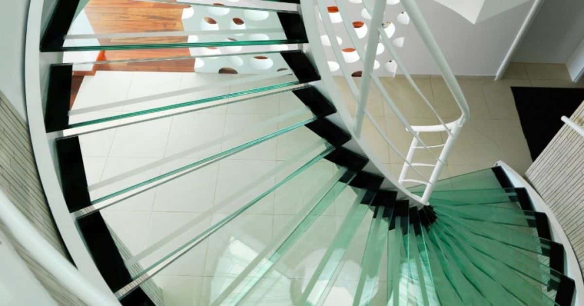 Stalen wenteltrap met glazen traptreden en witte balustrade of trapleuning.