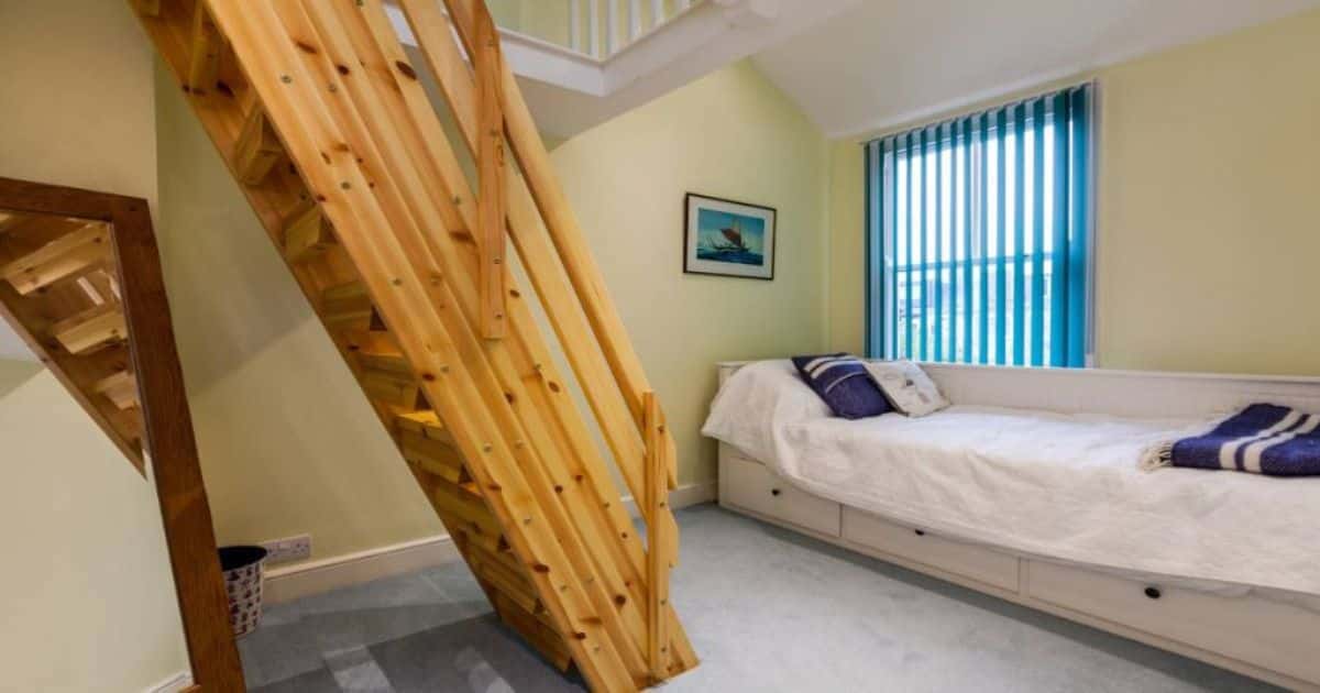 Steile houten trap met leuning in een slaapkamer of logeerruimte.