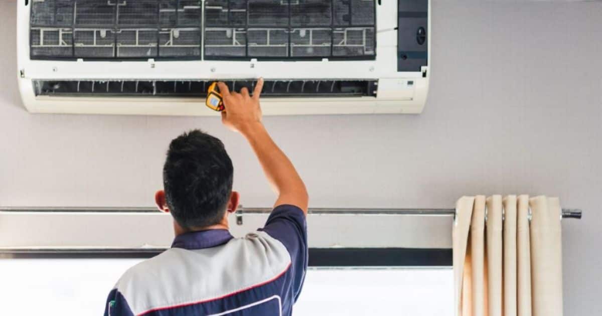 Een installateur in blauwe overall met blauwe pet installeert hier een grote witte airco wandunit.