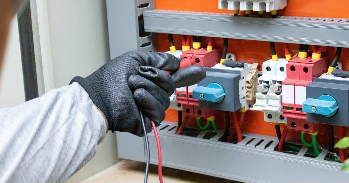 Een hand in een donkergrijze rubberen handschoen. De elektricien controleert de meterkast.
