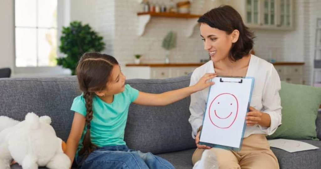 Een ergotherapeute houdt een klembord met daarop een blad vast. Het meisje kijkt ernaar en ziet een gezicht met een glimlach.