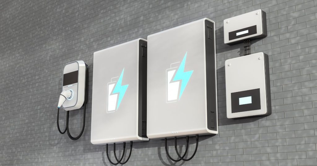 Een lichtgrijs energieopslagsysteem met 2 thuisbatterijen, omvormer en wallbox tegen een grijs betegelde wand.