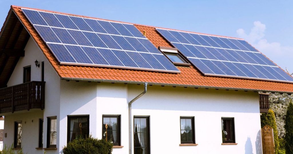 Huis met witte gevel en rood-oranje dakpannen: op het dak liggen langs weerszijden van het dakvenster telkens 24 zonnepanelen.