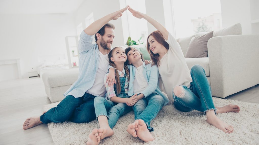Een gezin met familiale verzekering: vader en moeder houden hun handen samen boven de hoofden van dochter en zoon.