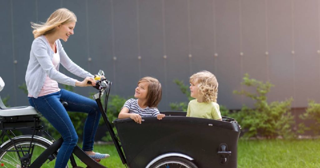 Een dame met zwarte bakfiets waar 2 kinderen in zitten, goed verzekerd met een fietsverzekering op maat.