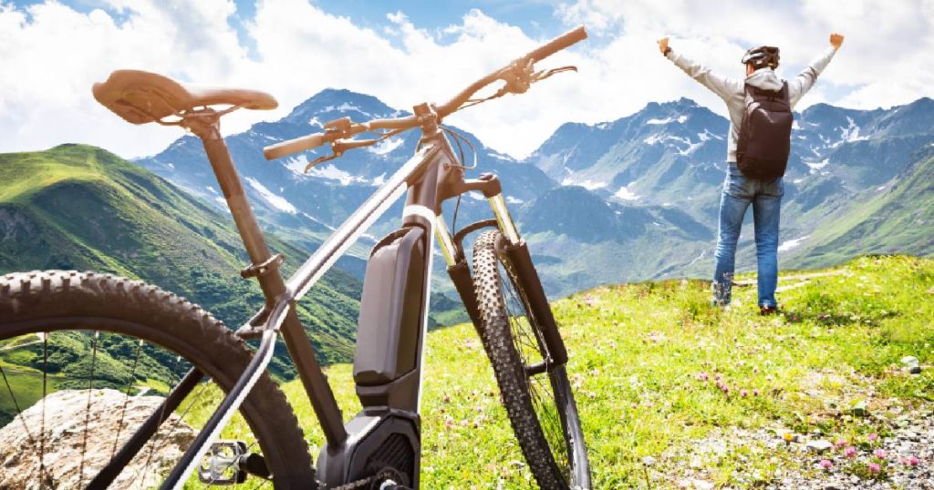 Een goed verzekerde elektrische fiets en een juichende man tegen een berglandschap.