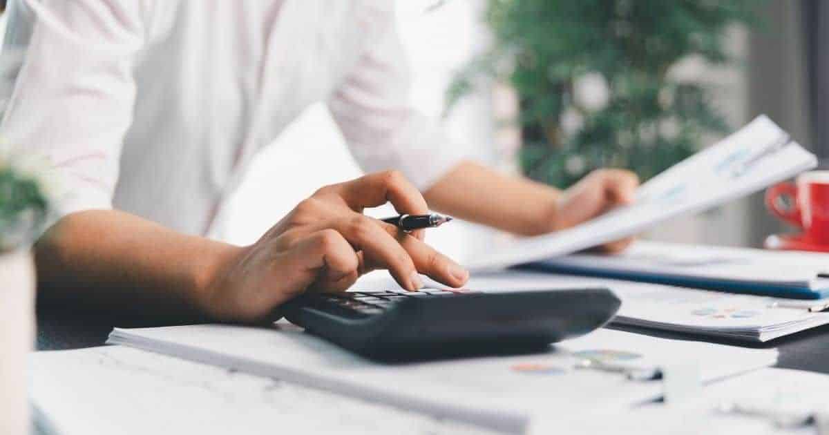 Een man die financiële documenten en kosten berekent met een zwarte rekenmachine.