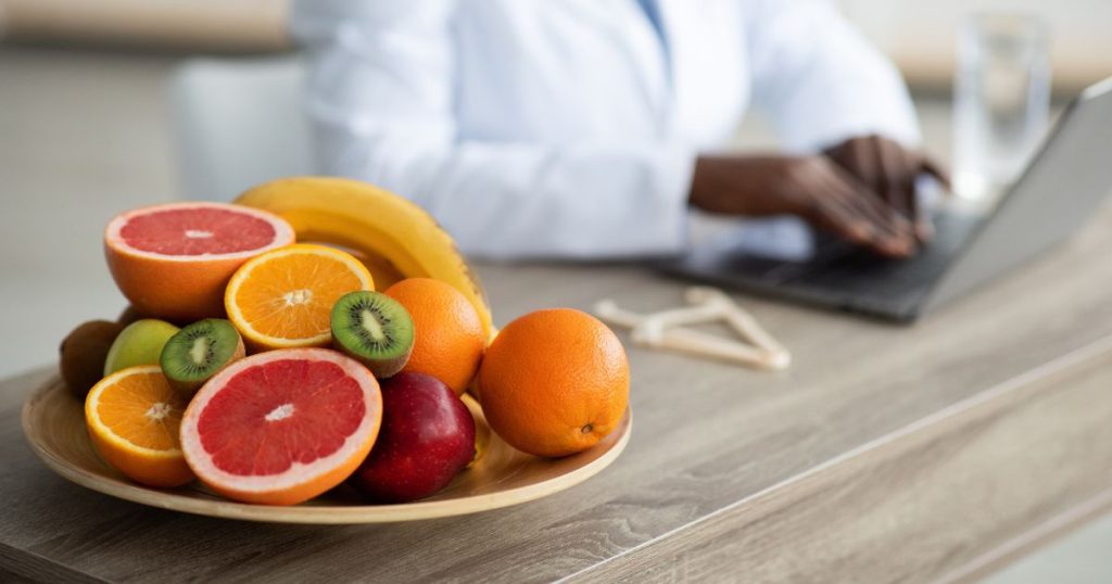 Een houten bord met fruit, waarvan zelfs een aantal gesneden. Op het bord liggen onder meer appelsienen, pompelmoezen, bananen en kiwi.