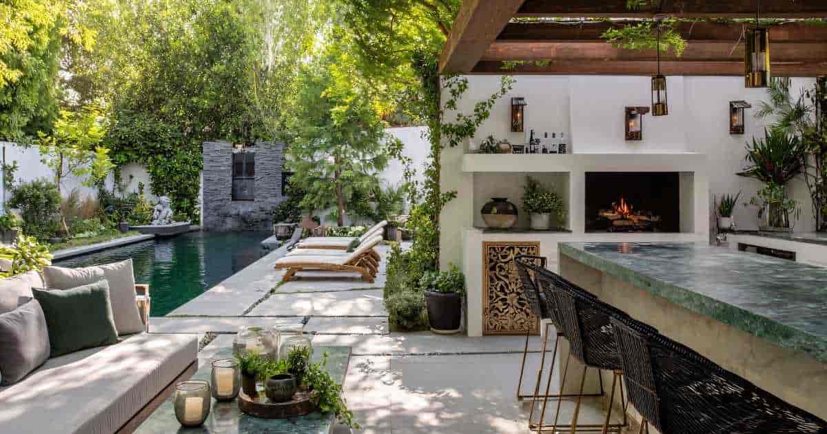 Een luxe terras met grote, lichte natuurstenen tegels, een zwembad, overkapping en bar. Het terras is omringd door planten en voorzien van loungezetels, ligstoelen en barkrukken.