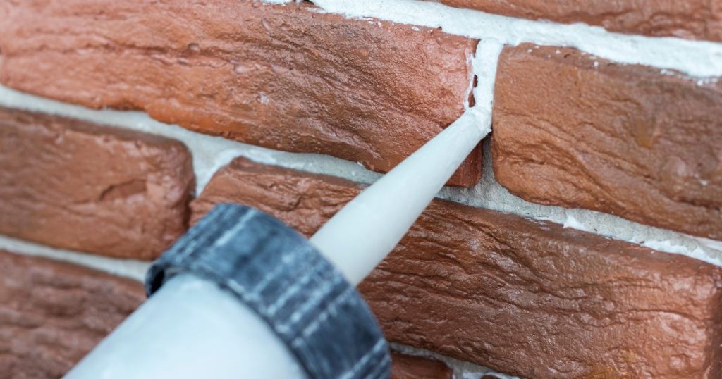 Detailbeeld van gevelstenen waartussen het grijze voegwerk wordt aangebracht met een voegpistool. 