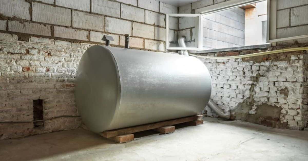 Een grijze, metalen stookolietank of mazouttank in een verluchte kelder met witte bakstenen muur en betonnen vloer.
