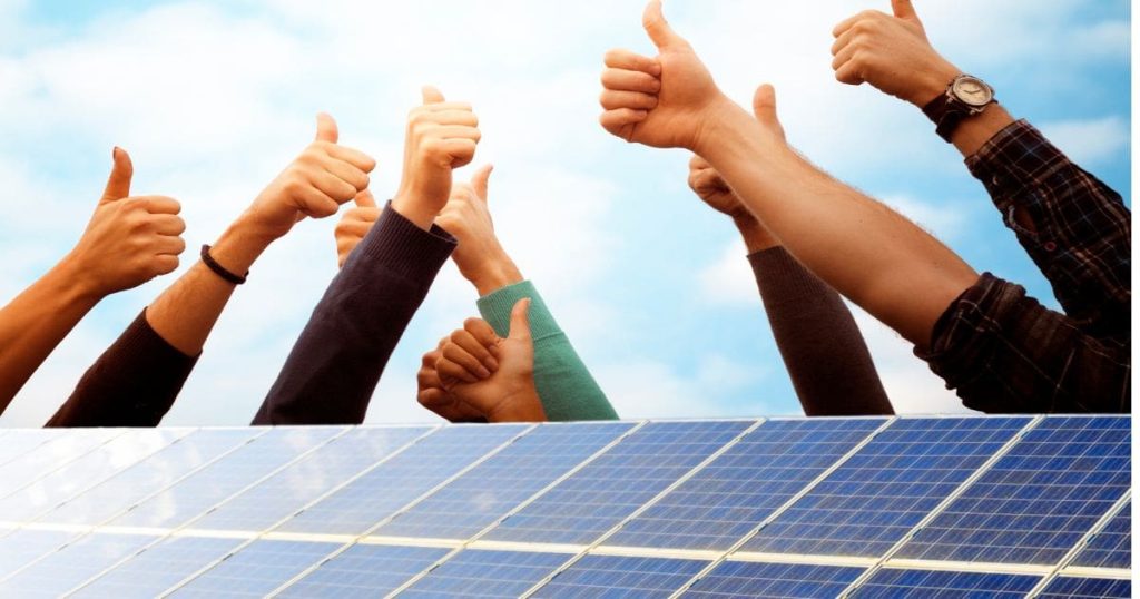 Een rij zonnepanelen met daarachter een rij mensen die hun duim omhoog steken.