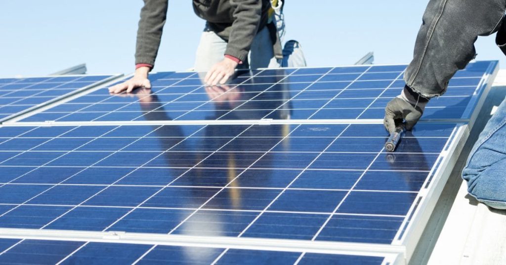 Twee installateurs zitten op een dak met zonnepanelen