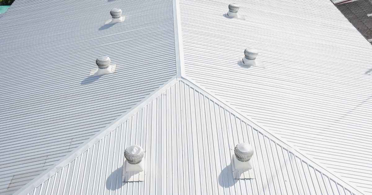 Het witte golfplaten dak van een industrieel gebouw. Zes verluchtingskanalen geven uit op het dak.