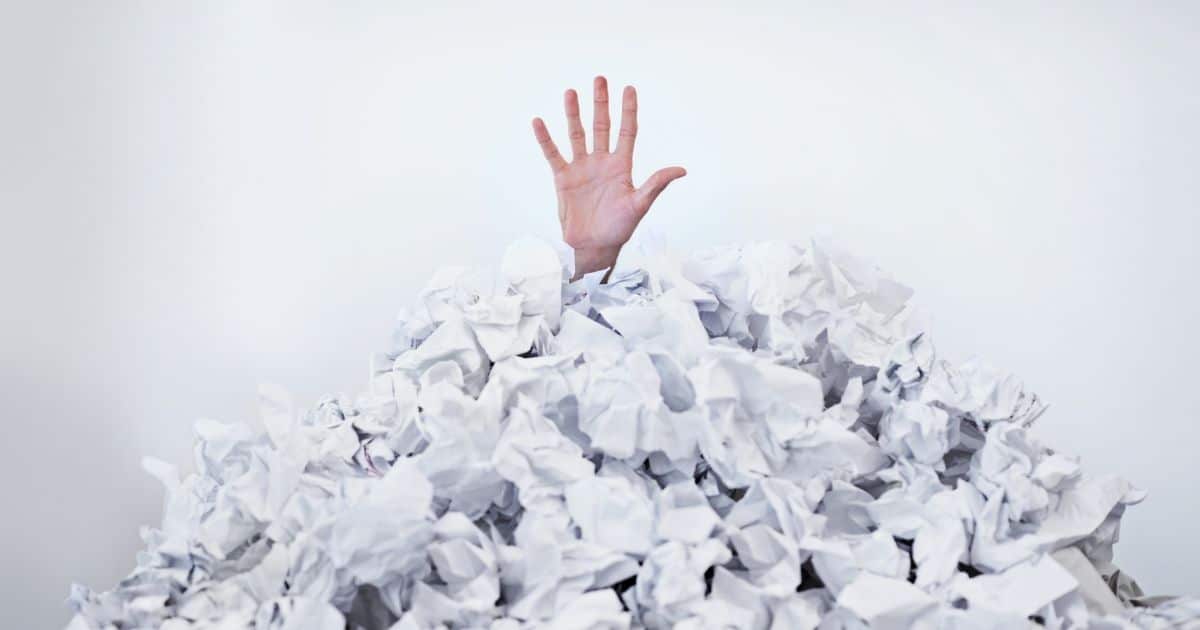 Een open handpalm met gespreide vingers steekt uit een hoop verfrommelde witte papieren.