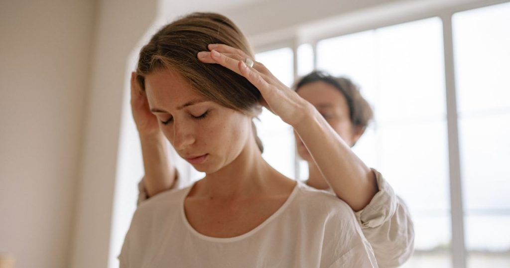 Een zorgverlener dient haptotherapie toe bij een vrouwelijke patiënt. Ze raakt het hoofd van de vrouw aan met beide handen.