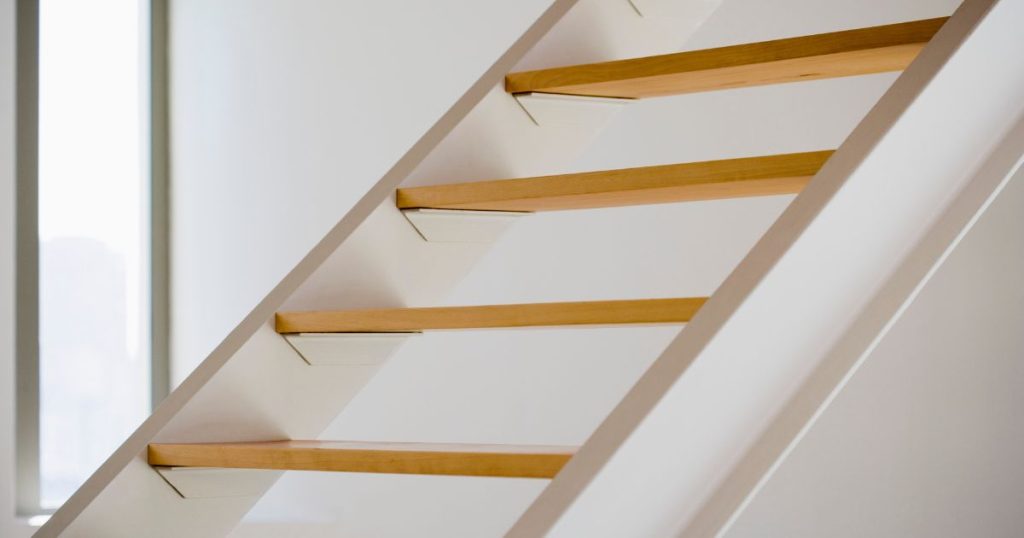 Een witte open trap met houten traptreden, met een vrij steile hellingshoek.