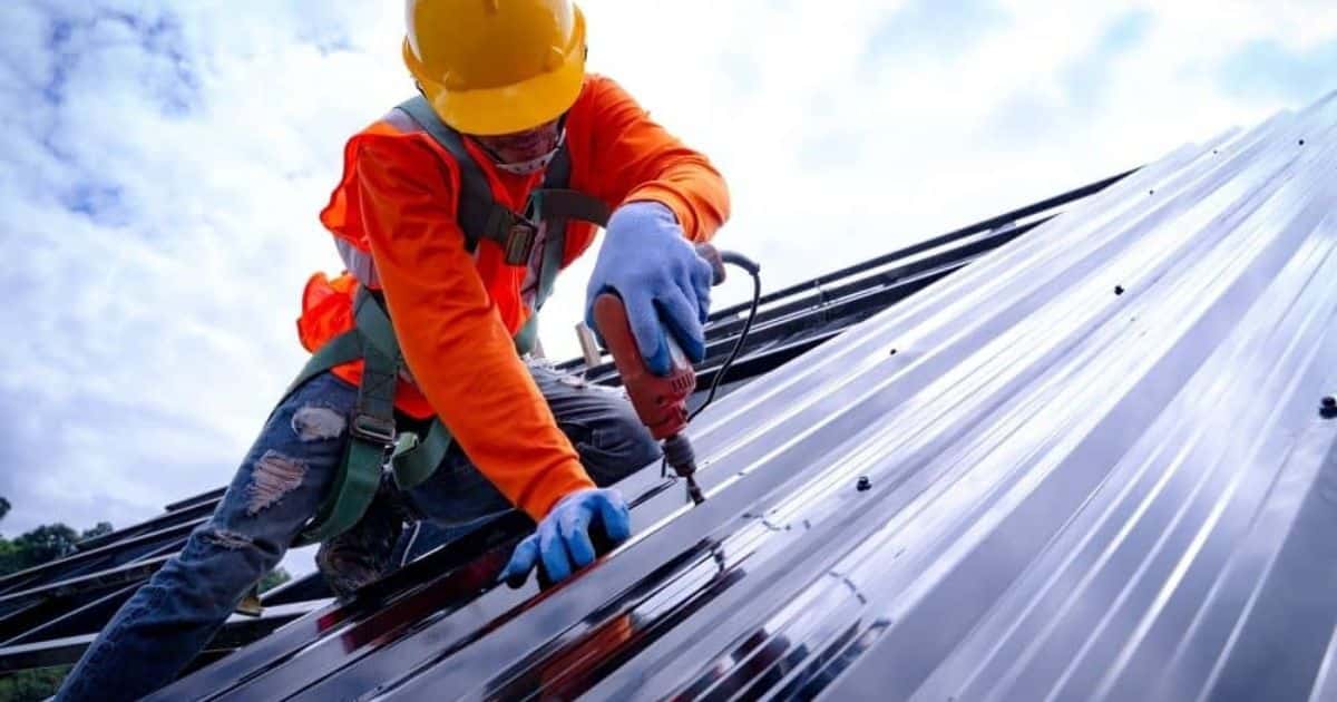 Een dakwerker plaatst zelfdragende geïsoleerde dakplaten met trapeziumprofiel op een stalen dakgebinte.