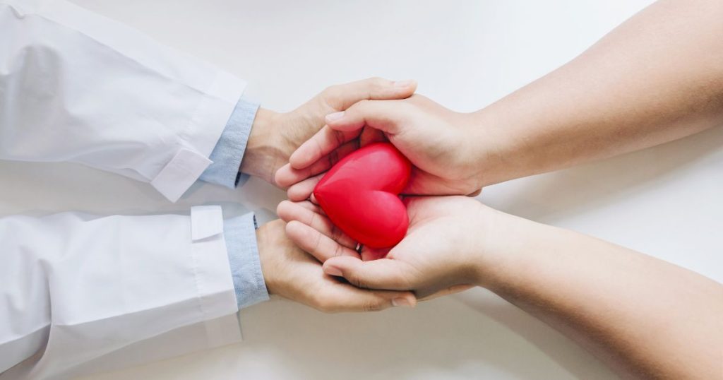 Twee handen van een jonge vrouw, met de palmen naar boven, in de handpalmen van een dokter. In de handen van de vrouw ligt een rood hartje.