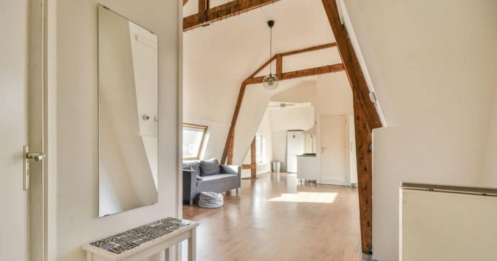 De binnenkant van een zolder onder een mansardedak, met zichtbare hanenbalken en gordingen.