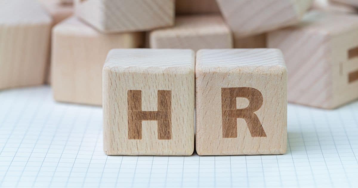 Twee houten blokken met de letters H en R. Op de achtergrond een stapel met meer houten blokken. Alle blokken liggen op een blad met kleine ruitjes.