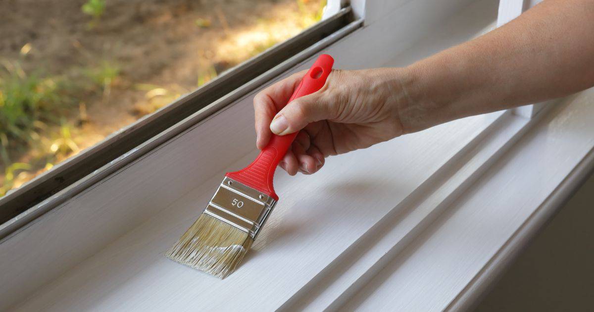 Een vakman schildert ramen met een witte verfkleur.