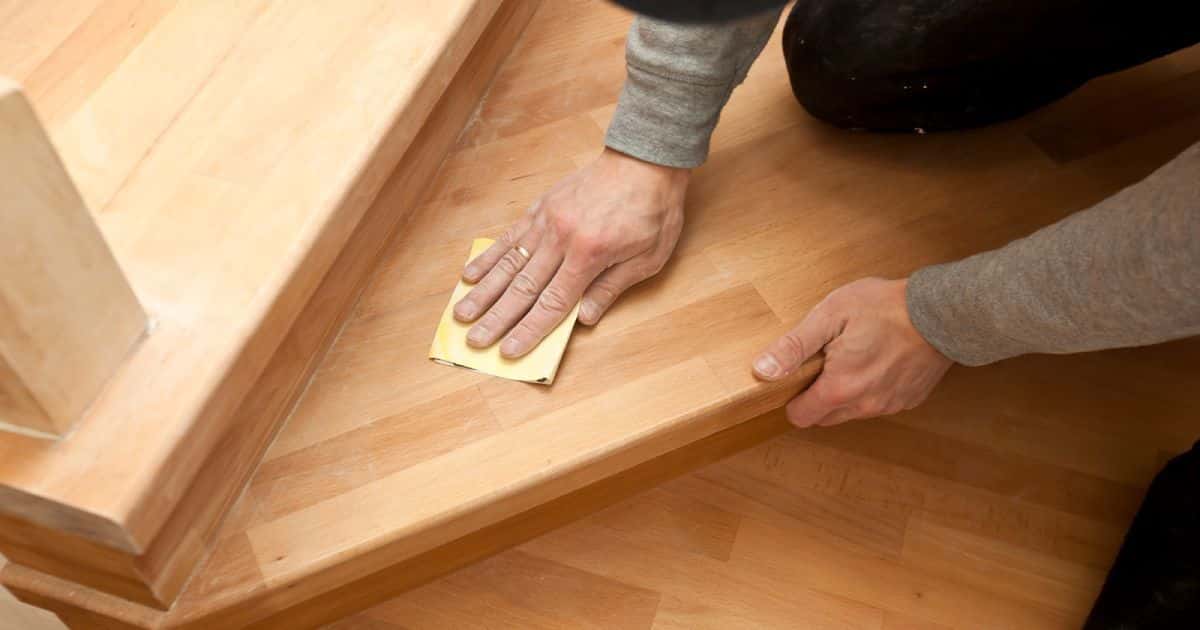 Een persoon die met een gele doek een houten trap is aan het kuisen. De persoon draagt een gouden ring. 