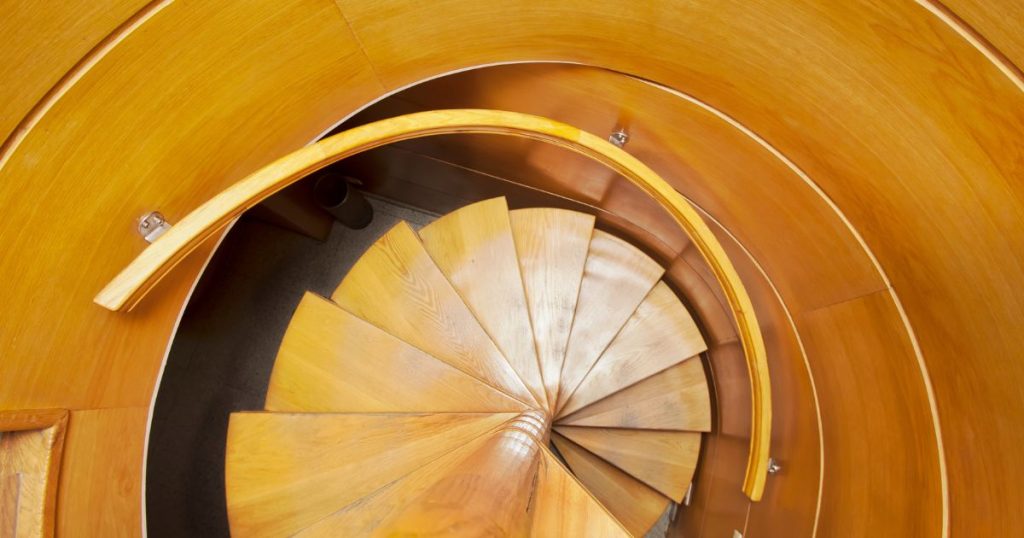 Een massief houten spiltrap met houten trapleuning en treden.
