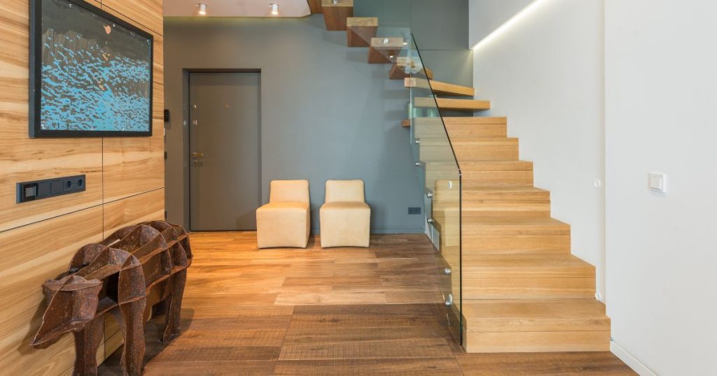 Een moderne houten trap met kwartslagdraai en glazen leuning. De traptreden zijn gesloten, tot halverwege de trap: vanaf daar zijn de treden open.