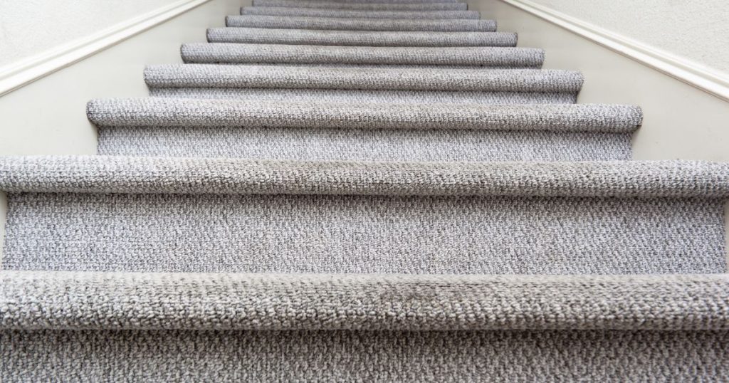 Een oude houten trap die men heeft laten renoveren en bekleden met grof, lichtgrijs traptapijt.