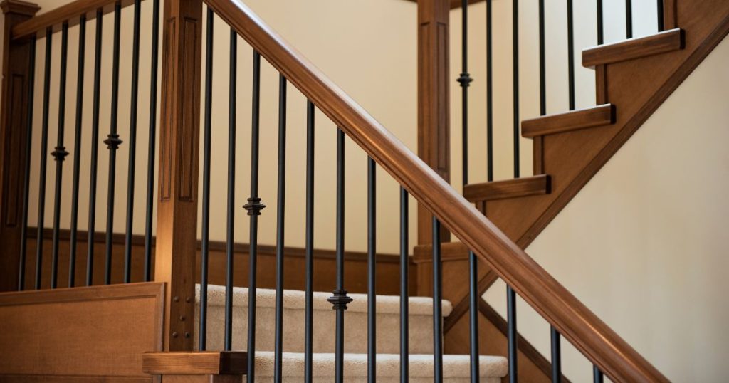 Een houten trap die men recent heeft laten renoveren door een specialist: een nieuwe trapleuning in hout en metaal en nieuw wit traptapijt.