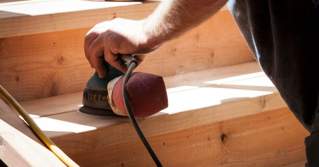 Een trapexpert gebruikt een schuurmachine om een houten trap te schuren als voorbereiding op het renoveren van de traptreden.