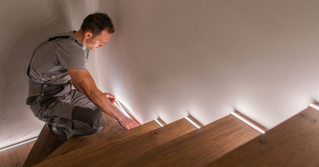 Een trapspecialist legt de laatste hand aan de afwerking van een trap door de plaatsing van ledverlichting langs de zijkant.