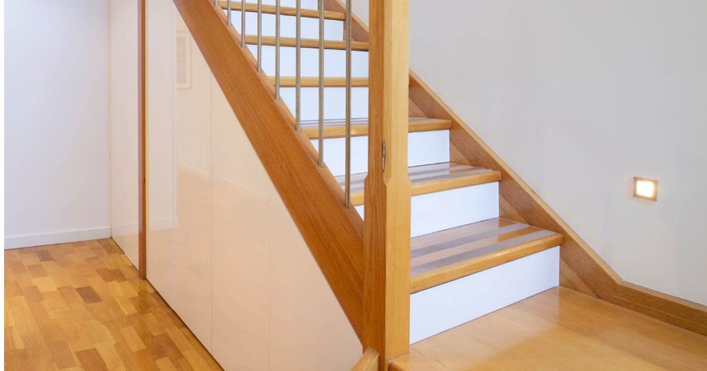 Een houten trap waarvan met de stootborden wit heeft laten schilderen. De treden zijn voorzien van antislip strips.