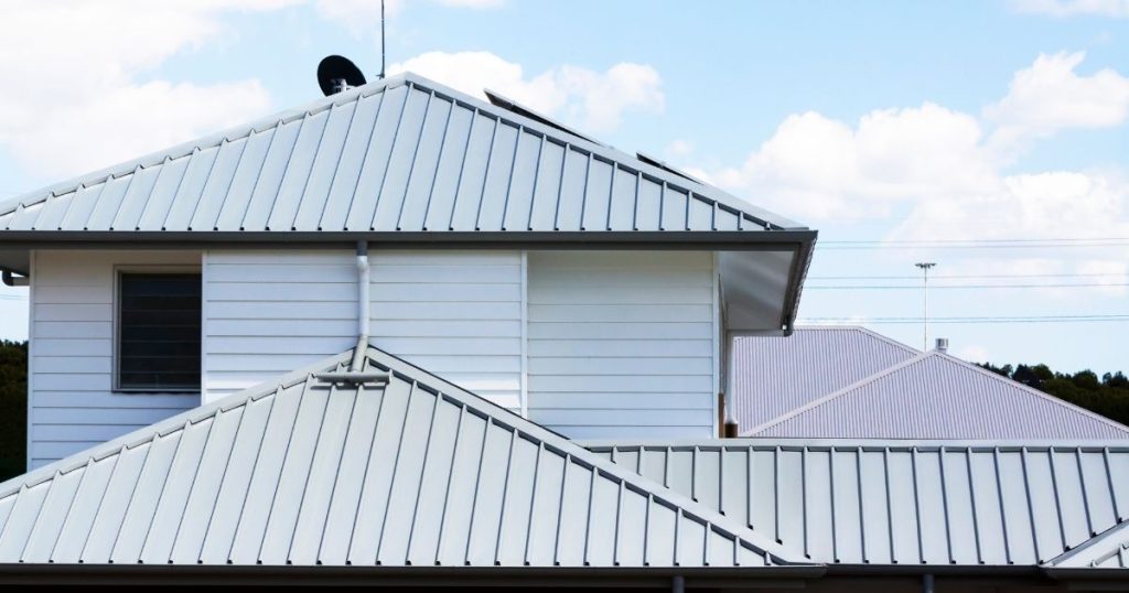 Een woning met witte gevel en lichtgrijs golfplaten dak.