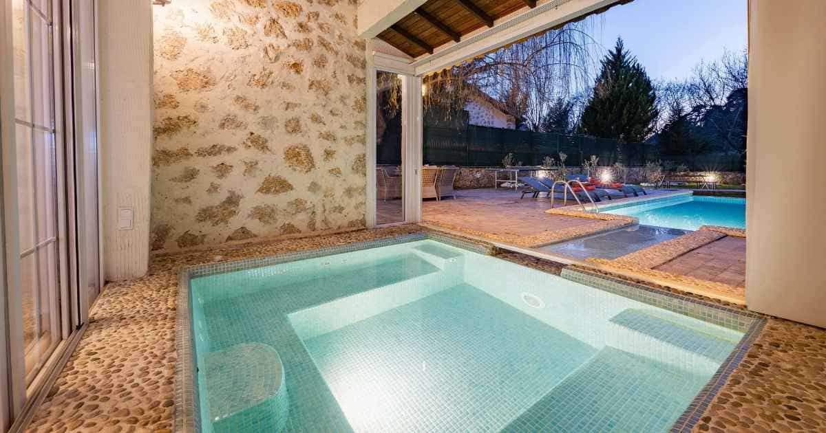 Een woning met binnenzwembad dat, met een smal kanaaltje, verbonden is met een buitenzwembad. Het binnenzwembad is omgeven door een vloer met kleine keitjes, het buitenzwembad is omrand met grote bruine tegels.